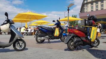 ukraina, kiev - 29 augusti 2020. massa parkerade mopeder med gula väskor med glovo-logga nära mcdonald's. budtjänst som levererar varor beställda via en mobilapplikation. redaktionell fotografering. foto