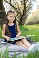 en barn flicka är läsning en bok i de parkera foto