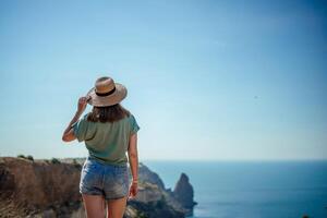 en kvinna bär en sugrör hatt står på en klippa utsikt de hav foto