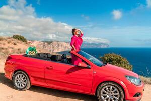 en kvinna är Framställ på topp av en röd bil. hon är bär en rosa kostym och solglasögon. foto