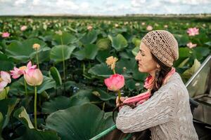 en kvinna är Sammanträde i en båt i en fält av rosa lotus blommor. hon är bär en hatt och en scarf. foto
