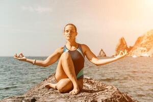 yoga på de strand. en Lycklig kvinna mediterar i en yoga utgör på de strand, omgiven förbi de hav och sten berg, främja en friska livsstil utomhus i natur, och inspirerande kondition begrepp. foto