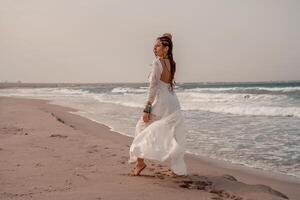 modell i boho stil i en vit lång klänning och silver- Smycken på de strand. henne hår är flätad, och där är många armband på henne vapen. foto