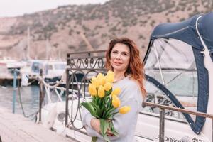 kvinna innehar gul tulpaner i hamn med båtar dockad i de bakgrund., mulen dag, gul Tröja, bergen foto