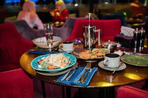 en tabell med en blå tallrik av sallad och en kopp av kaffe. de tabell är uppsättning med bestick och en få koppar. scen är tillfällig och inbjudande, som den är en restaurang miljö med människor njuter deras måltider. foto