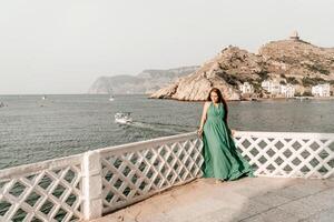kvinna hav grön klänning. sida se en Lycklig kvinna med lång hår i en lång mynta klänning Framställ på en strand med lugna hav bokeh lampor på solig dag. flicka på de natur på blå himmel bakgrund. foto