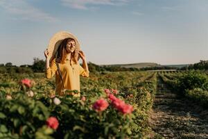 en kvinna bär en sugrör hatt står i en fält av rosa blommor. hon är leende och hon är njuter de skön landskap. foto