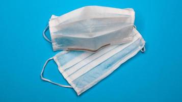 två kirurgiska engångsmasker med gummikuddar för att täcka mun och näsa på blå bakgrund. begreppet skydd mot bakterier, sjukvård och medicin. covid19. kopieringsutrymme foto
