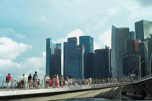 singapore, augusti 19, 2023-gruppen av människor gående på de bro med fullt med folk av hög modern byggnader i bakgrund foto