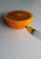 de nål av en spruta halv fylld med orange juice genomborrar de skala av en mogen orange. frukt testa begrepp bild foto