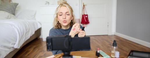 porträtt av ung kvinna bloggare, skönhet smink vloggare, som visar läppstift färgrutor på henne hand, rekommenderar kosmetika till henne följare, skapande innehåll för social media konto på digital kamera foto