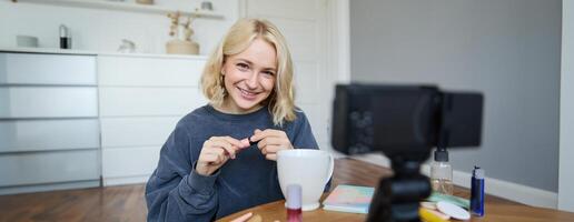 porträtt av ung leende kvinna i henne rum, inspelning på kamera, livsstil vlog för social media, innehav mascara, granskning henne smink skönhet Produkter, som visar på vilket sätt till använda sig av kosmetika foto