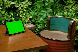 grön skärm ipad eller läsplatta på trä- tabell med grön växter bakgrund foto