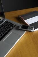 telefon, bärbar dator och tom anteckningsbok på skrivbordet foto