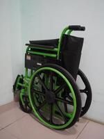 en grön hopfällbar rullstol lutande mot en vit vägg. de rullstol är betitlad till de sida med de vänster hjul vilar mot de vägg foto