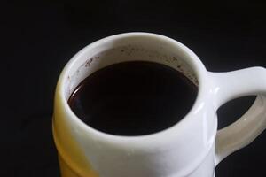 närbild Foto av svart kaffe i vit och gul kopp på svart keramisk tabell
