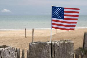 utah strand i Normandie, Frankrike. USA flagga på trä hav staket. sand, hav och molnig himmel. foto