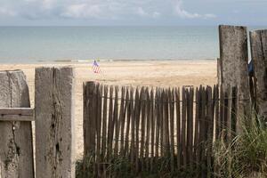 utah strand i Normandie, Frankrike. USA flagga på trä hav staket. sand, hav och molnig himmel. foto