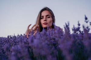 kvinna lavendel- fält. Lycklig sorglös kvinna i beige klänning och hatt med stor brätte lukta en blomning lavendel- på solnedgång. perfekt för inspirera och värma begrepp i resa och reslust. stänga upp foto