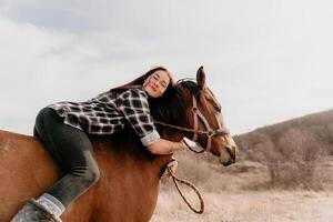 ung Lycklig kvinna i hatt med henne häst i kväll solnedgång ljus. utomhus- fotografi med mode modell flicka. livsstil humör. begrepp av utomhus- ridning, sporter och rekreation. foto