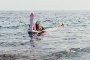 ung Lycklig kvinna i vit bikini och bär rosa mask får redo för hav snorkling. positiv leende kvinna avkopplande och njuter vatten aktiviteter med familj sommar resa högtider semester på hav. foto