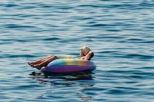 sommar semester kvinna flyter på ett uppblåsbar munk madrass, en vatten leksak simma ringa. positiv Lycklig kvinna avkopplande och njuter familj sommar resa högtider semester på de hav. långsam rörelse foto