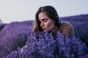 kvinna lavendel- fält. Lycklig sorglös kvinna i beige klänning och hatt med stor brätte lukta en blomning lavendel- på solnedgång. perfekt för inspirera och värma begrepp i resa och reslust. stänga upp foto