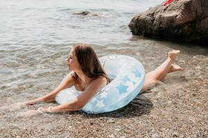 kvinna sommar hav. Lycklig kvinna simning med uppblåsbar munk på de strand i sommar solig dag, omgiven förbi vulkanisk berg. sommar semester begrepp. foto