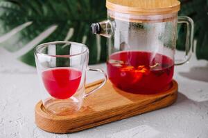 nyligen bryggt hibiskus te i glas tekanna och kopp foto