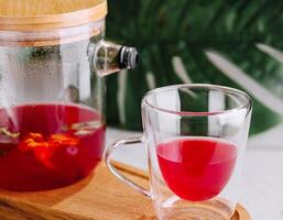 nyligen bryggt hibiskus te i glas tekanna och kopp foto