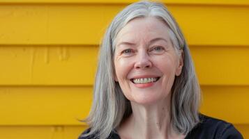 leende kvinna med grå hår i främre av gul vägg foto