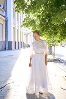 elegant mitten ålder kvinna i en vit årgång klänning mot de bakgrund av historisk byggnader i de morgon- ljus foto