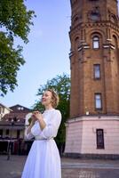 chic ung kvinna i en vit årgång klänning på de fyrkant nära de historisk vatten torn i vinnytsia foto