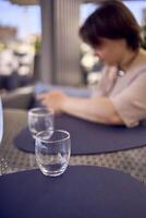 plus storlek kvinna i persika ludd klänning väljer en maträtt i en restaurang via qr koda i smartphone, vatten med citron- och glasögon i främre av henne foto