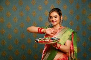 porträtt av en trevlig kvinna i saree innehav tallrik av diya i en diwali festival foto