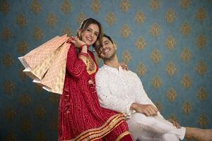 stock bild av en Make och fru bär traditionell klädespersedlar Framställ i främre av de kamera innehav handla påsar under de diwali festival foto