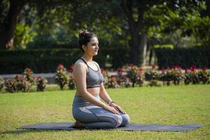 en ung kvinna lärare är håller på med vajrasana asana i de parkera. foto