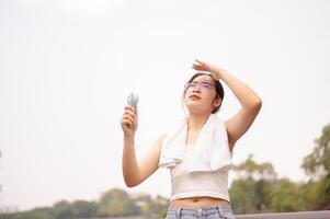 en kvinna innehar en små fläkt och våtservetter henne svettas på henne ansikte medan gående utomhus på en varm dag. foto