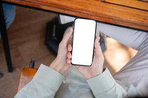 en man använder sig av hans smartphone på en tabell i en Kafé, med en vit skärm smartphone mockup. foto