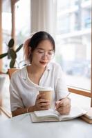 en ung asiatisk kvinna högskola studerande är håller på med läxa i en kaffe affär. foto