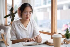 en ung asiatisk kvinna högskola studerande är håller på med läxa i en kaffe affär. foto