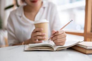 en beskurna skott av en kvinna skrivning något i henne anteckningsbok medan Sammanträde i en kaffe affär. foto