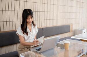 en affärskvinna är arbetssätt avlägset från en kaffe affär, arbetssätt på henne bärbar dator och tar anteckningar. foto