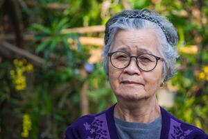 porträtt av en senior kvinna med kort grå hår bär glasögon, leende, och ser på de kamera medan stående utomhus. Plats för text. begrepp av åldrig människor och sjukvård foto