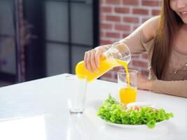 närbild av kvinna hand häller orange juice in i en glas. friska livsmedel begrepp foto