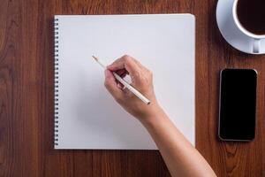 närbild av hand kvinna innehav en penna förbereda för teckning på skissbok placerad på trä- tabell. trä textur bakgrund. begrepp av teckning och teknologi foto