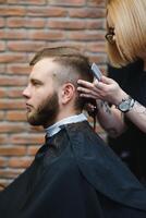 eleganta man Sammanträde barberare affär hårstylist frisör kvinna skärande hans hår porträtt stilig Lycklig ung skäggig caucasian kille få trendig frisyr attraktiv barberare flicka arbetssätt tjänande klient. foto