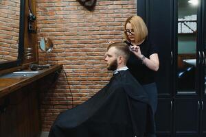 eleganta man Sammanträde barberare affär hårstylist frisör kvinna skärande hans hår porträtt stilig Lycklig ung skäggig caucasian kille få trendig frisyr attraktiv barberare flicka arbetssätt tjänande klient foto