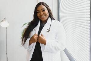 porträtt av skön leende kvinna afrikansk amerikan läkare stående i medicinsk kontor. hälsa vård begrepp, medicinsk försäkring, kopia Plats foto