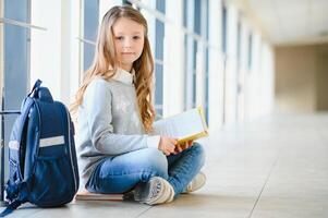 främre se av Söt blond skola flicka innehav många färgrik anteckningar och böcker. duktig tonåring flicka leende på kamera, stående på korridor av internationell skola. foto